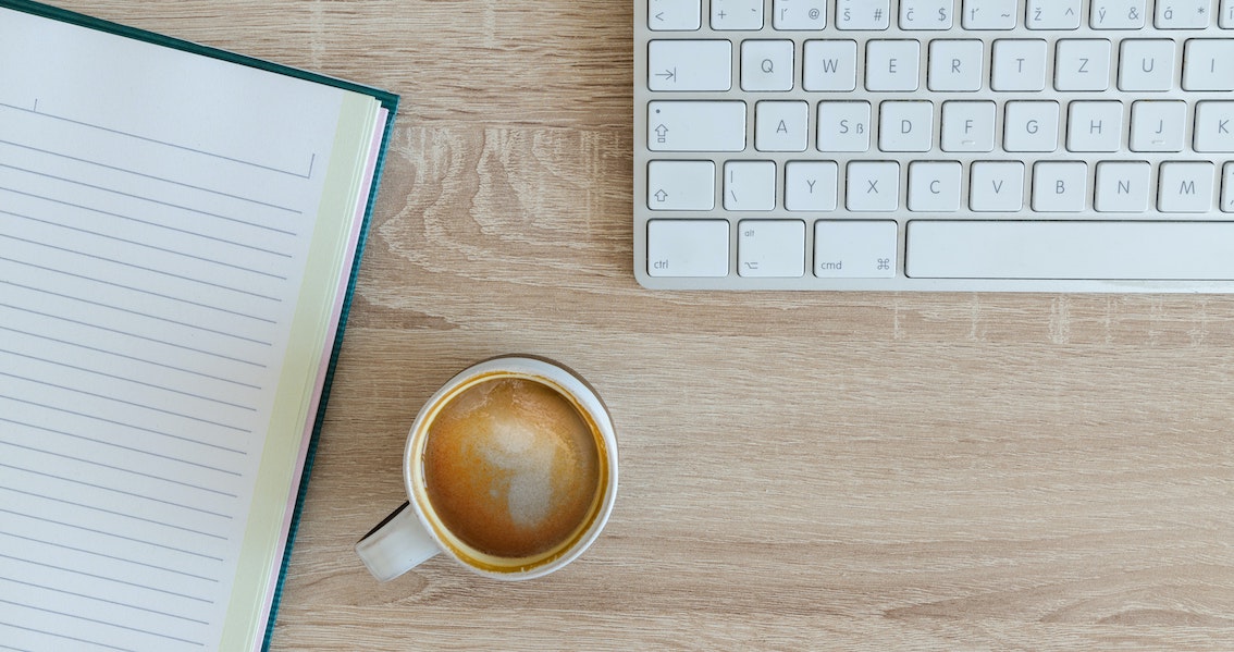 Coffee next to notepad and keyboard.